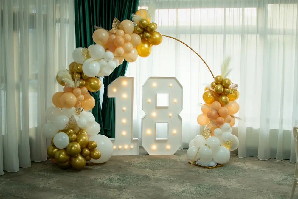 A lit-up number 18 sign with gold and white balloons