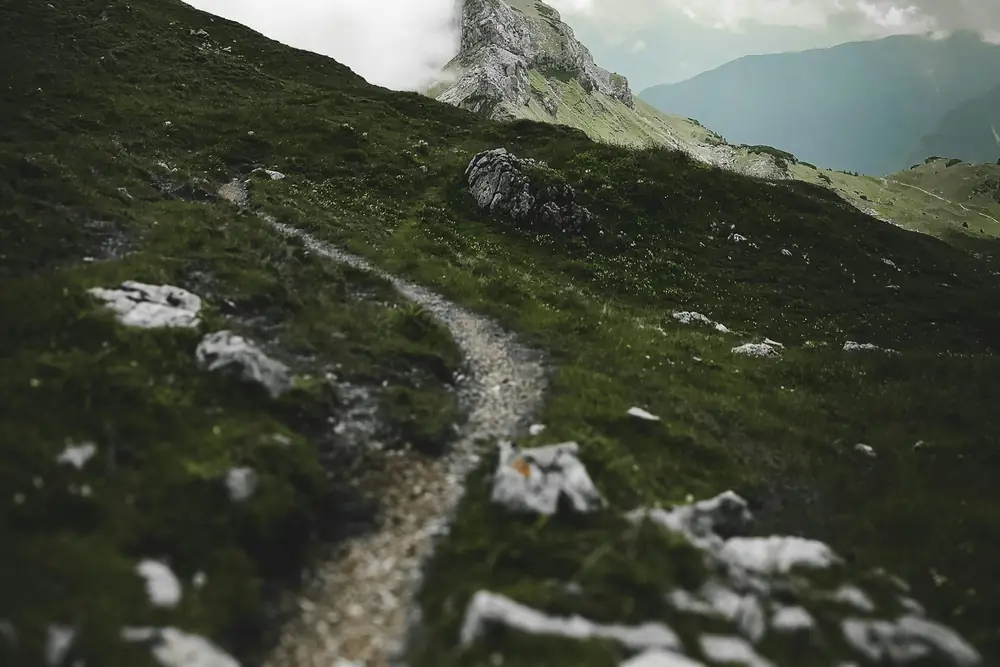 A trail climbing a green mountain ridge under clouds