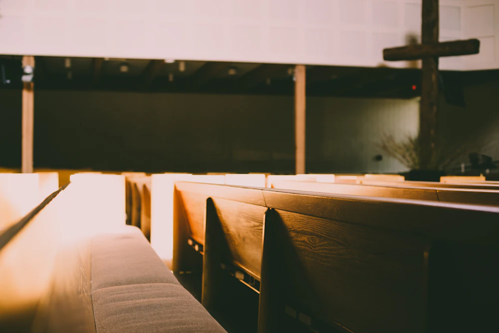 Wooden church pews in soft morning light with a cross on the wall
