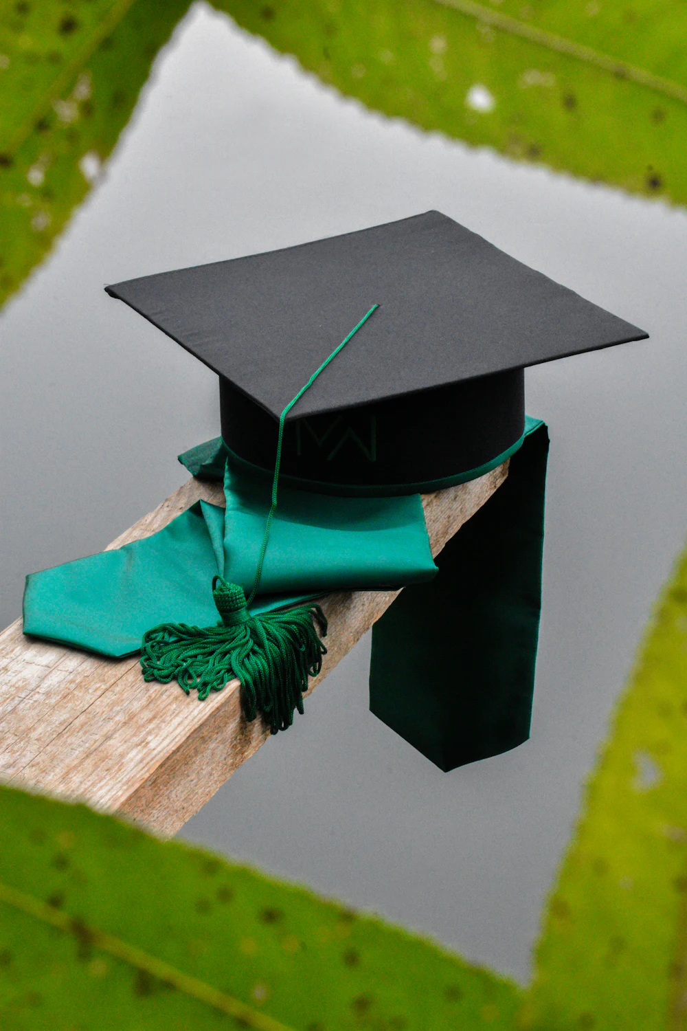 A black graduation cap with a green tassel resting on a wooden beam