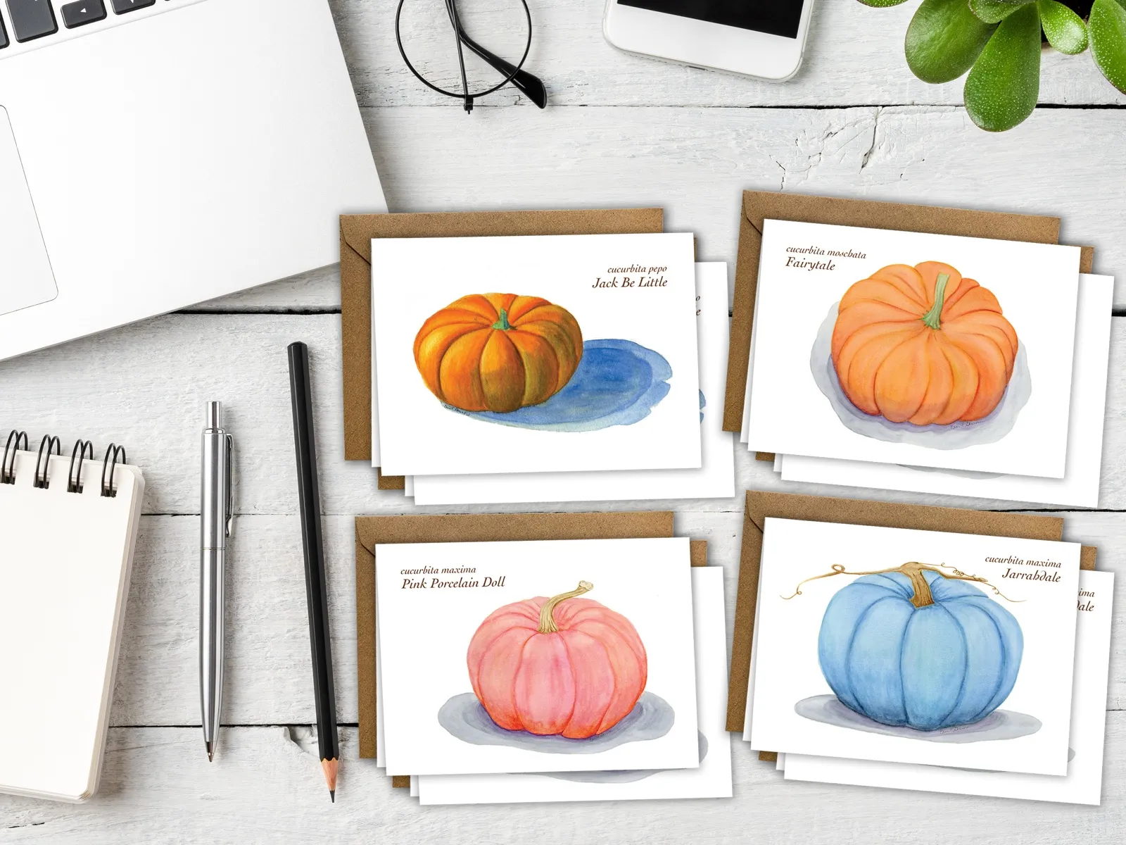 Four watercolor pumpkin greeting cards with kraft envelopes on a white desk.