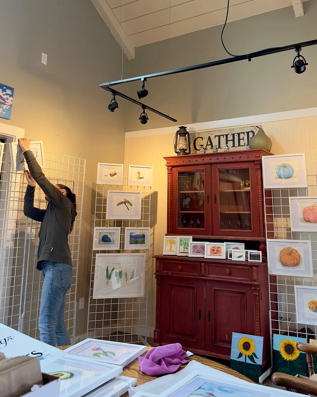 Erin hanging watercolor paintings on a gallery wall while setting up her Open Studios space.