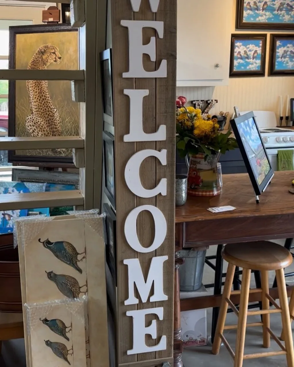A tall wooden WELCOME sign beside framed watercolors in the Kasten Family Wines studio space.
