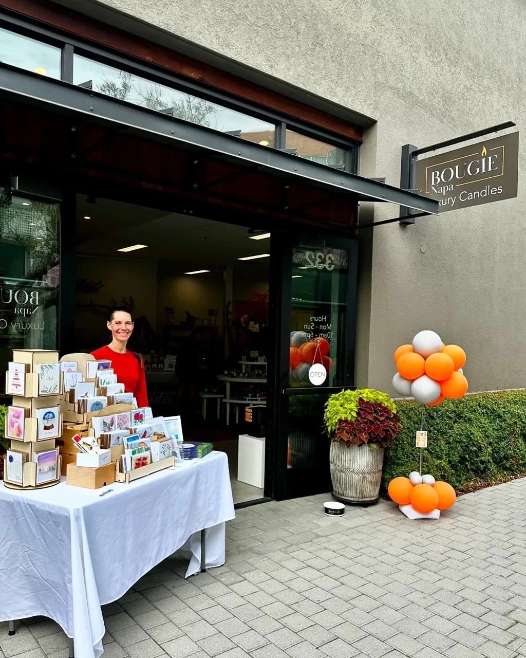 Erin standing at her table of cards and prints outside the Bougie pop-up store, with orange balloons.