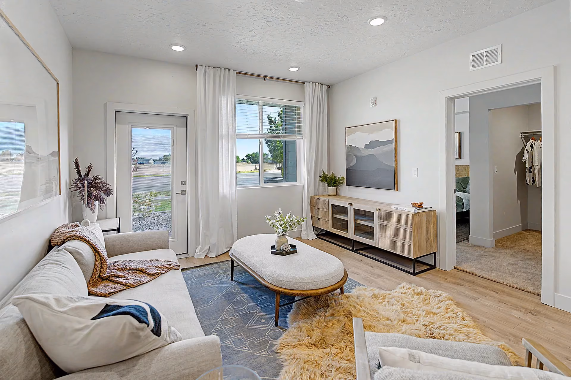 Furnished living room with large window, patio view, and bedroom entry