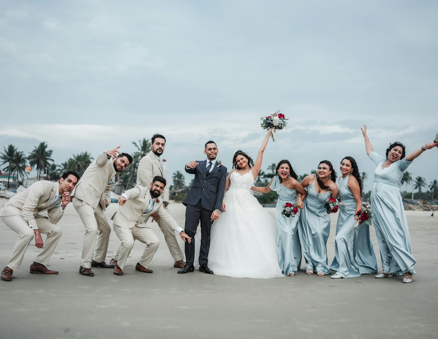 A bride and groom celebrating with their laughing wedding party on the beach