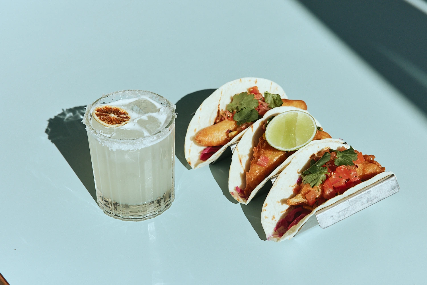 Three tacos with lime beside a salt-rimmed margarita at The Pav
