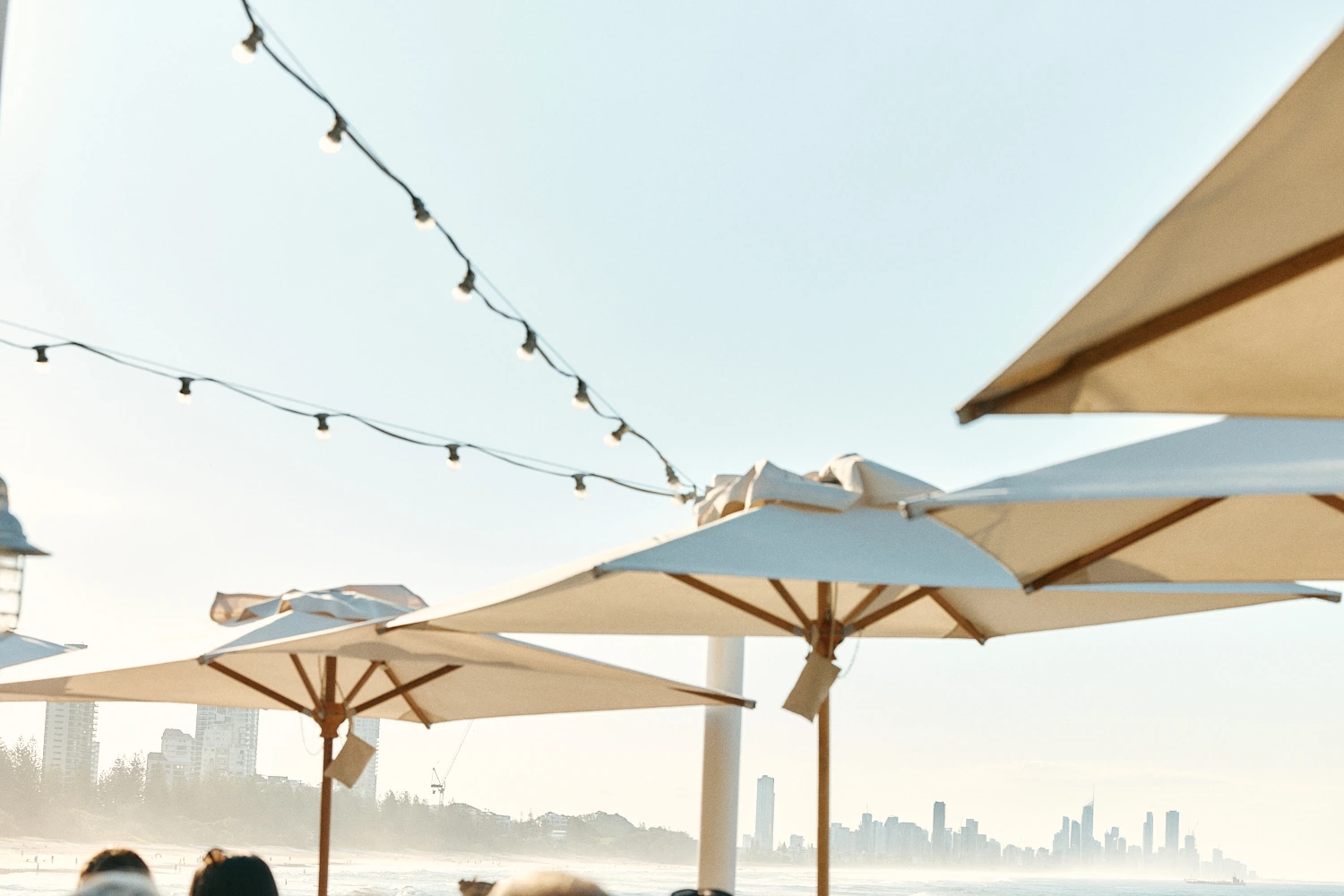 Festoon lights strung above white umbrellas, with the city skyline in the haze