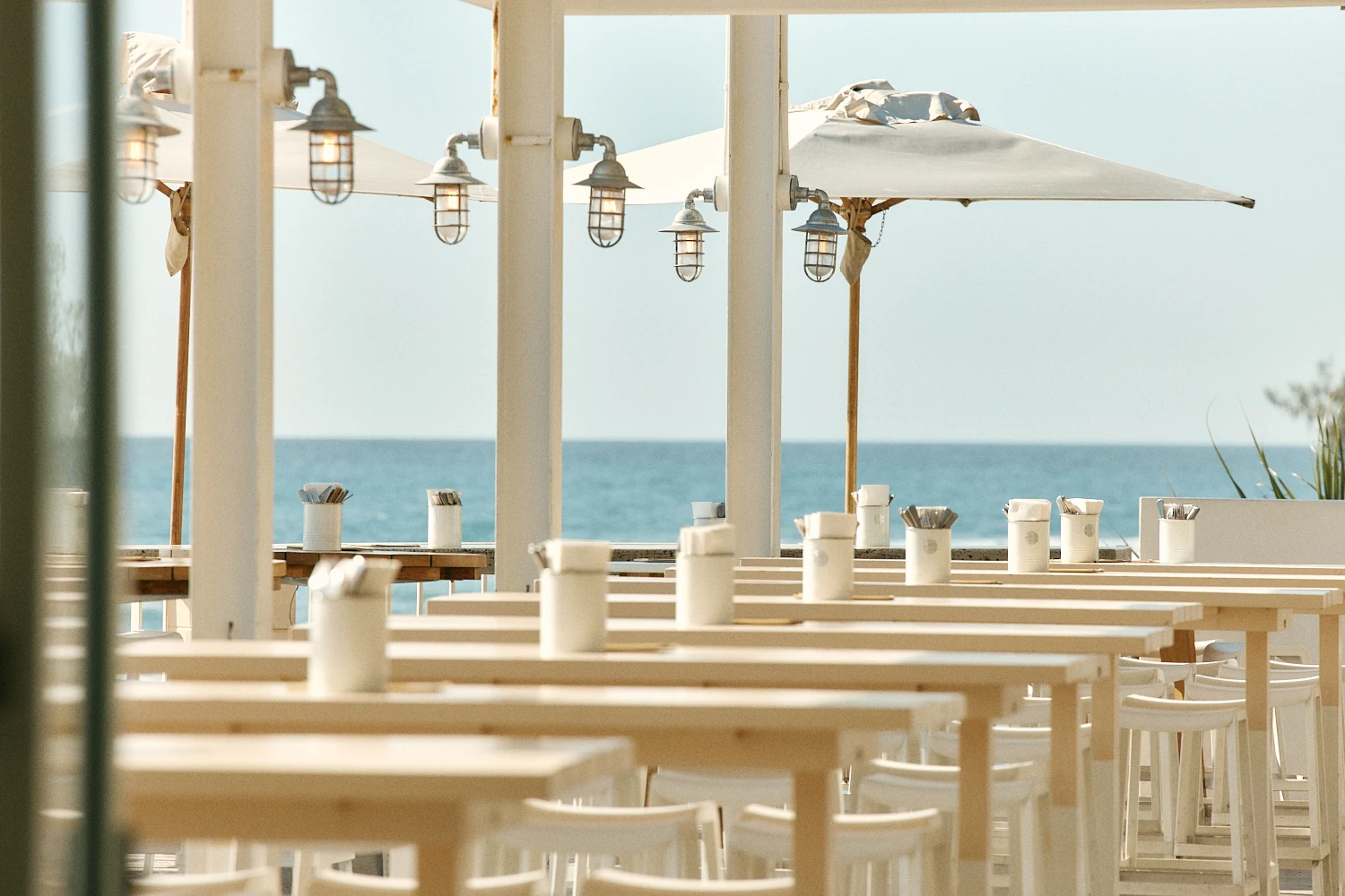 Timber tables under lanterns and umbrellas with the ocean behind