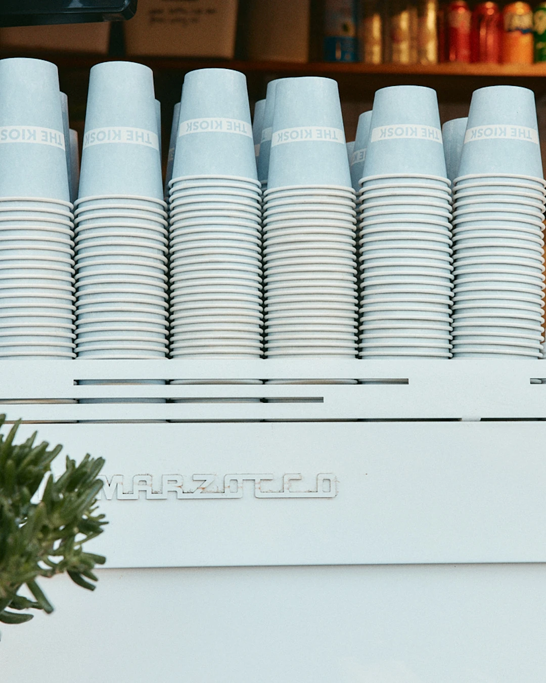 Stacks of The Kiosk coffee cups on top of the espresso machine