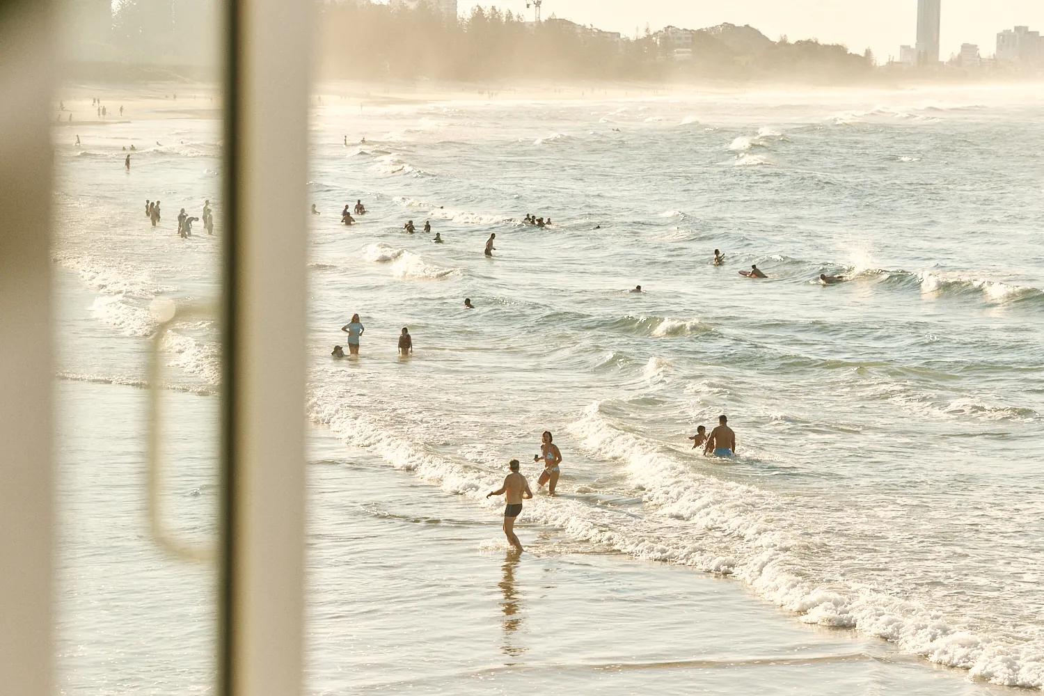 Swimmers in the golden afternoon surf at Burleigh Beach, seen through a window