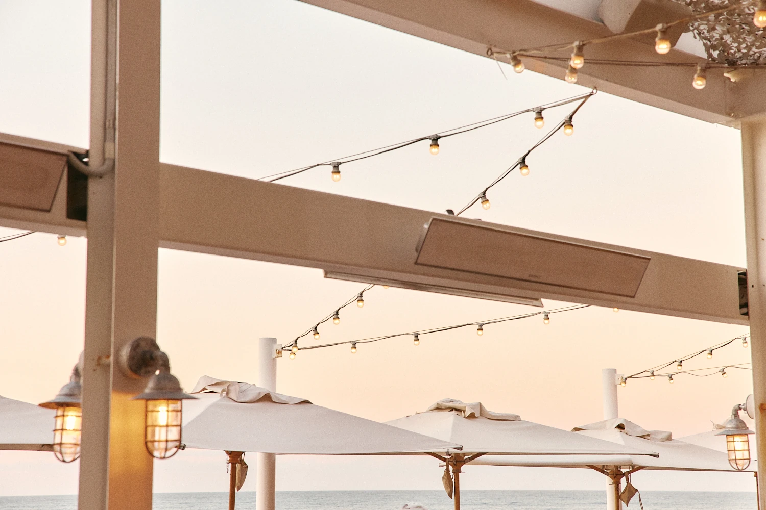 Festoon lights and lanterns glowing over terrace umbrellas at dusk