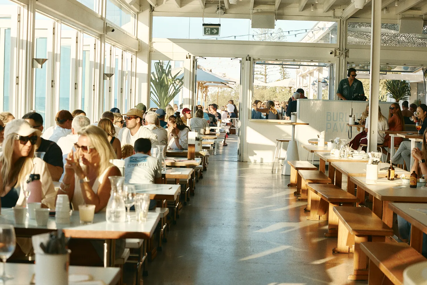 Guests dining at long timber tables inside Burleigh Pavilion