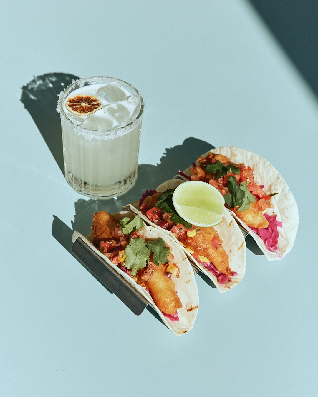 Three tacos with lime beside a salt-rimmed margarita at The Pav