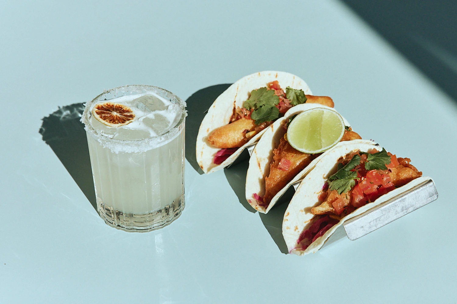 Three tacos with lime beside a salt-rimmed margarita at The Pav