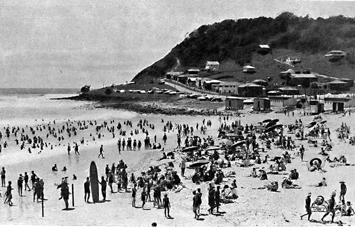 Black and white photo of a busy Burleigh Heads beach with swimmers and early beach shacks