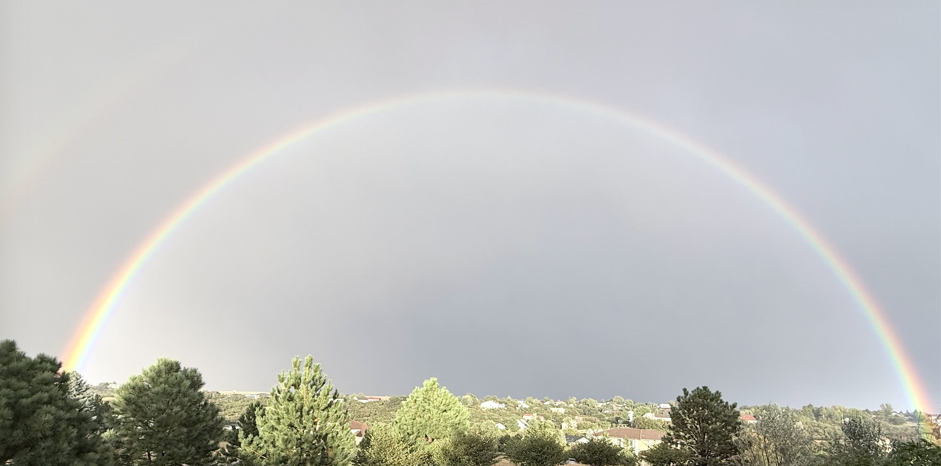 A full double rainbow arcing over the pines and foothills of Charter Oaks