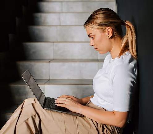 A woman sits on some stairs using a laptop