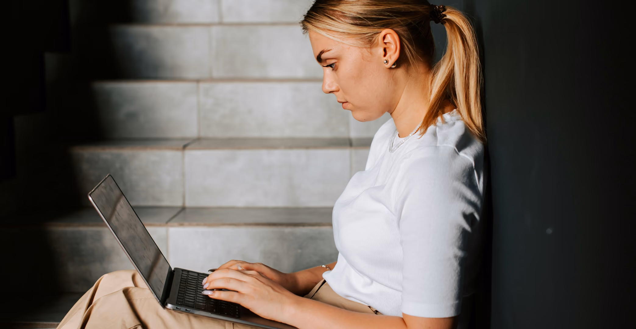 A woman sits on some stairs using a laptop