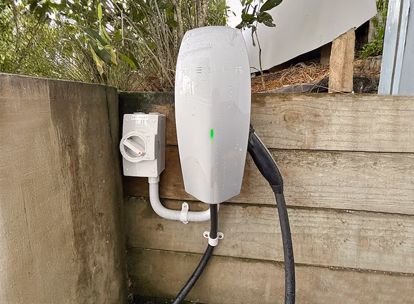 Wall-mounted EV charger and isolator fixed to a timber retaining wall