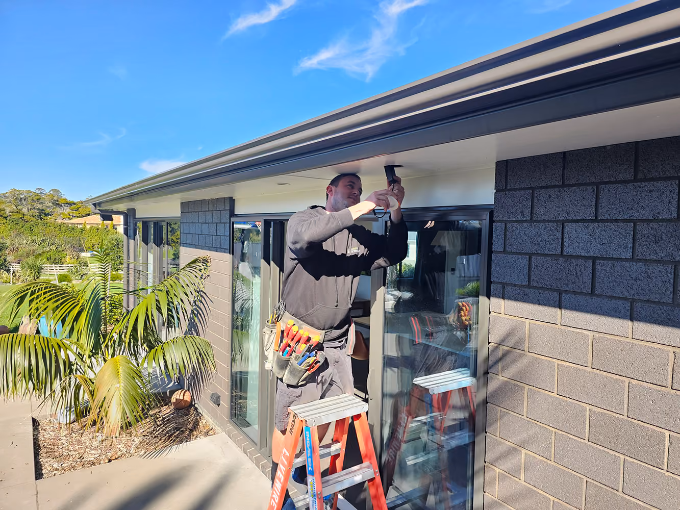 Livewire electrician on a ladder wiring an exterior fitting on a block home