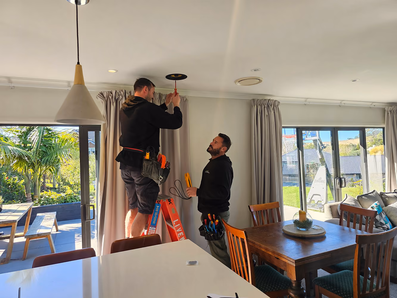 Two Livewire electricians fitting a ceiling fixture in a dining room