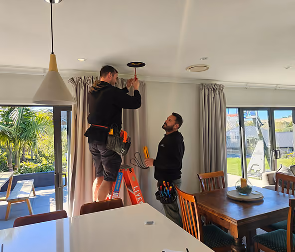 Two Livewire electricians installing a ceiling light fitting in an Auckland living room
