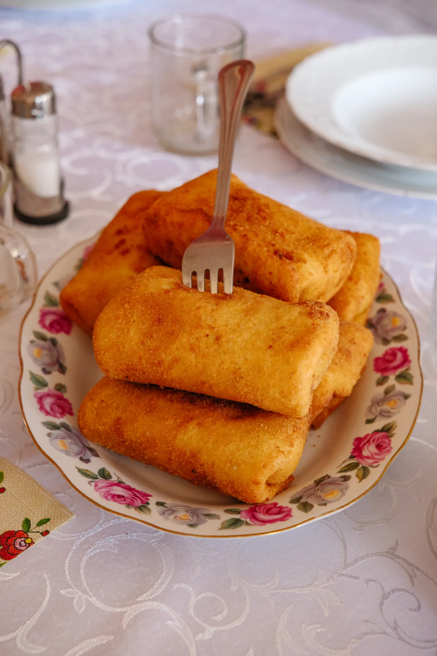 Plate of golden fried breaded krokiety with a fork resting on top, on a floral china plate on a white lace tablecloth.