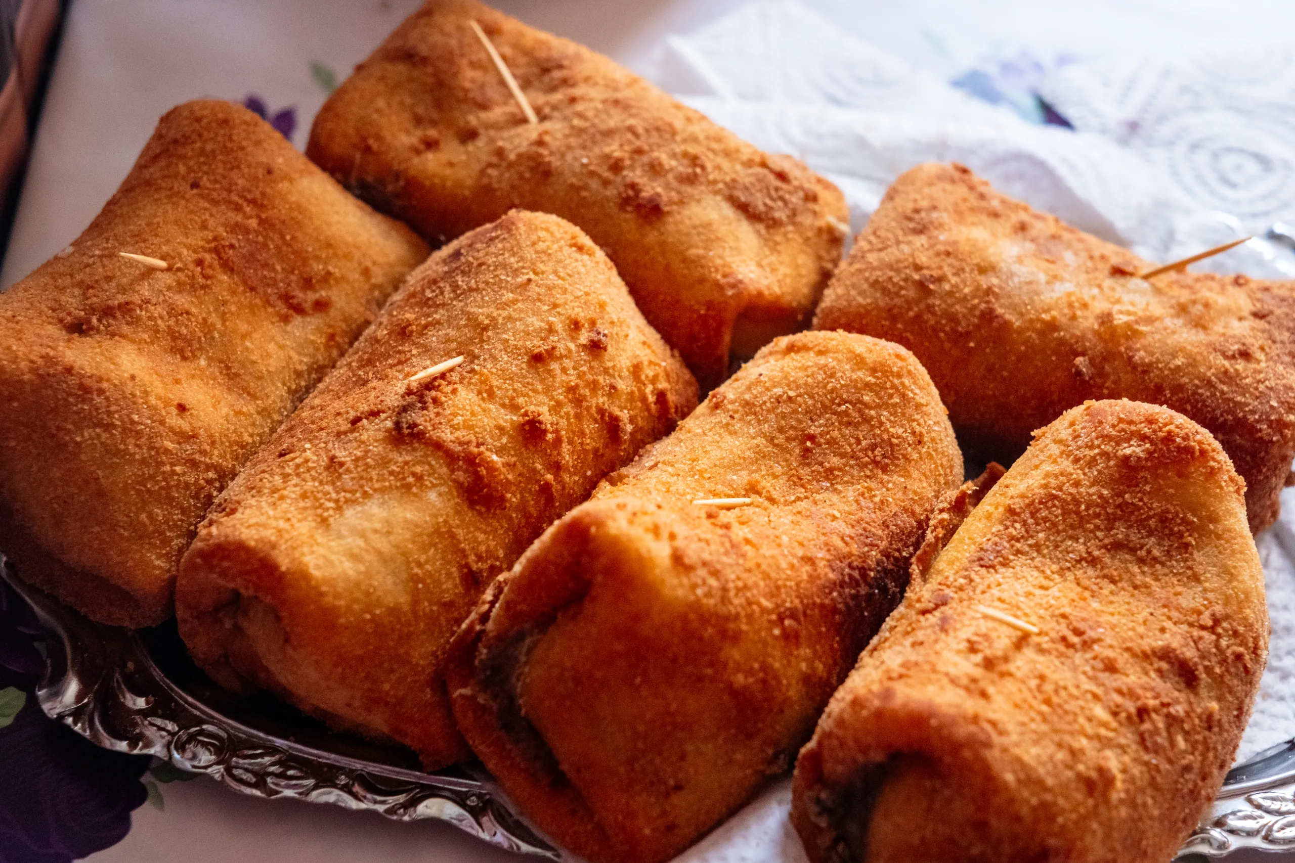 Close-up of six breaded and fried krokiety pancake rolls on a silver platter.