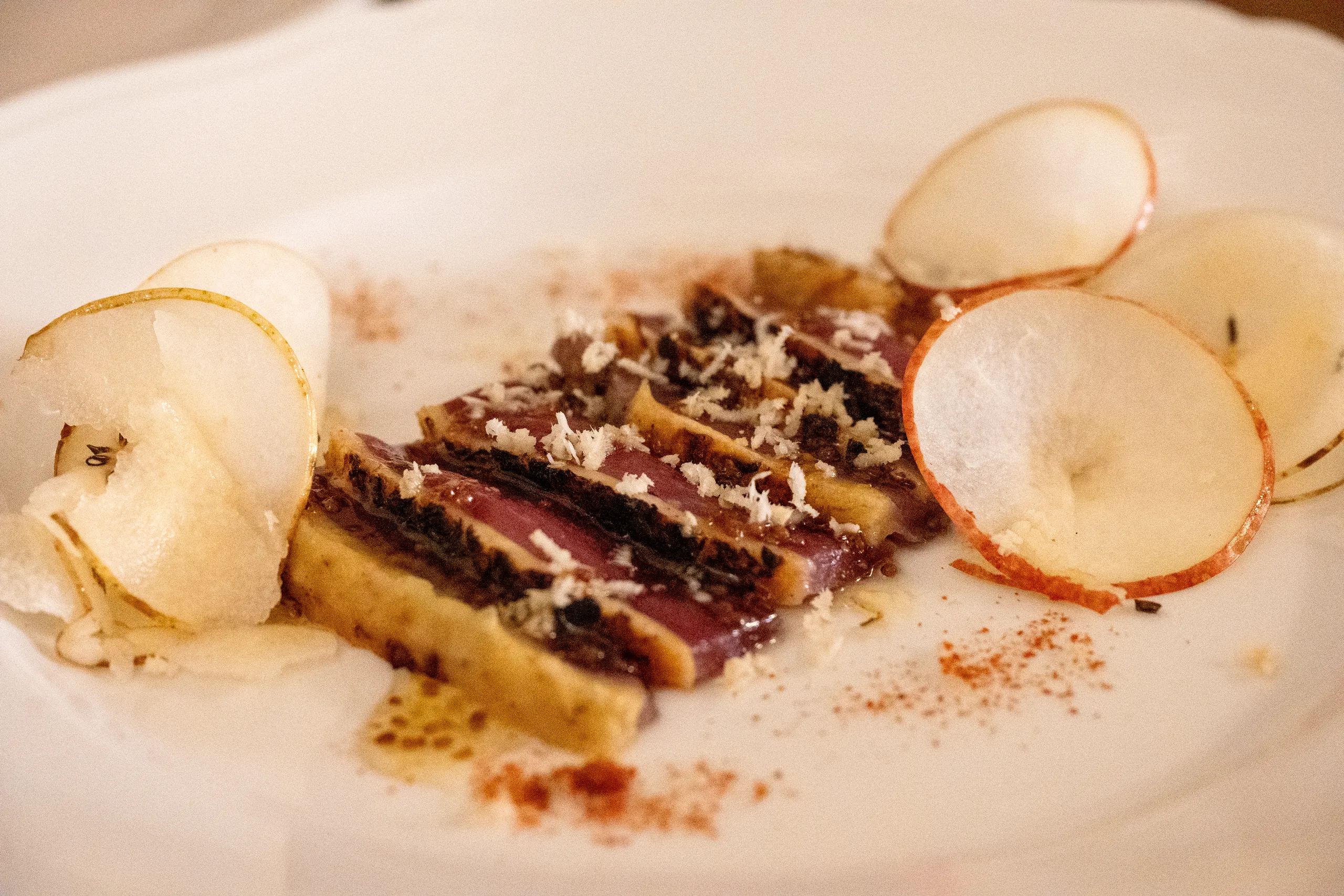 Slices of seared rare tuna with grated cheese and paprika on a white plate, with thin rounds of fresh pear arranged around them.