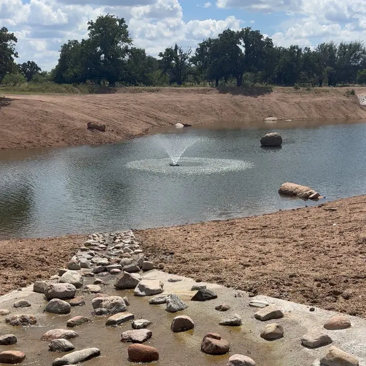 Ranch pond with a fountain and rock-lined spillway built by Flying G Excavation