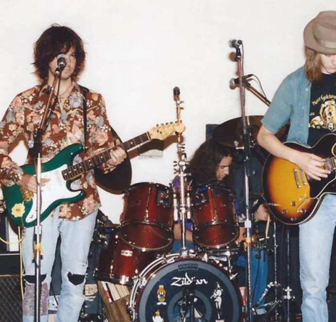 Early band photo, two guitarists with a drummer behind them