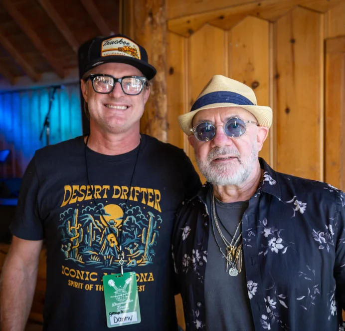 Two friends smiling backstage in a wood-paneled room