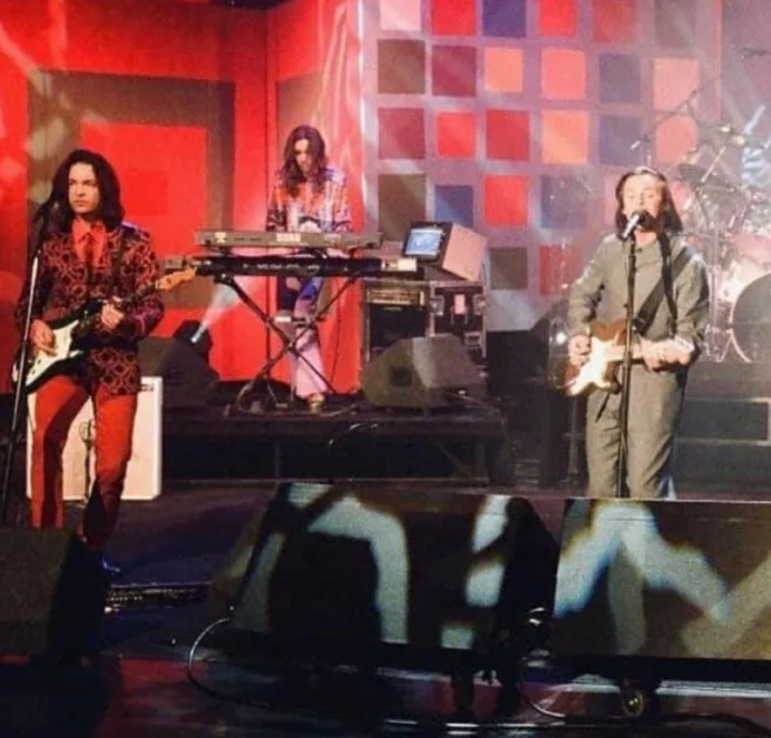 Band performing on a TV stage set with a red, checkered backdrop