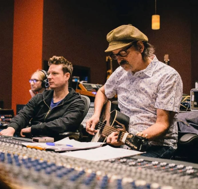 Playing acoustic guitar at a large mixing console in a recording studio