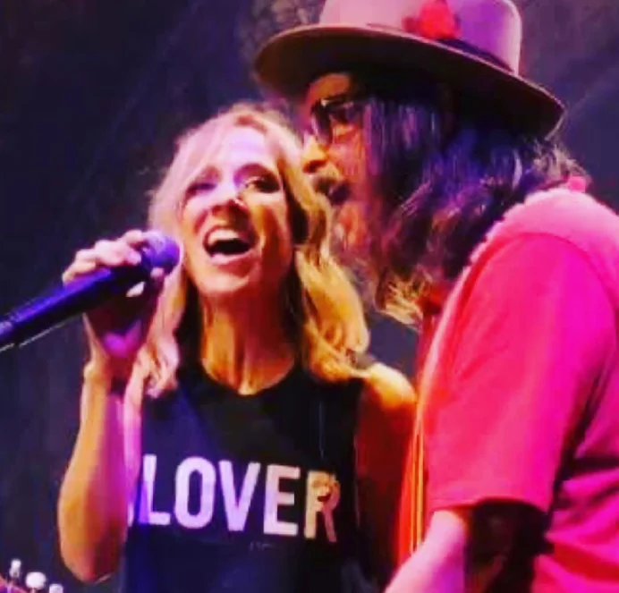 Two singers sharing one microphone on stage under pink light