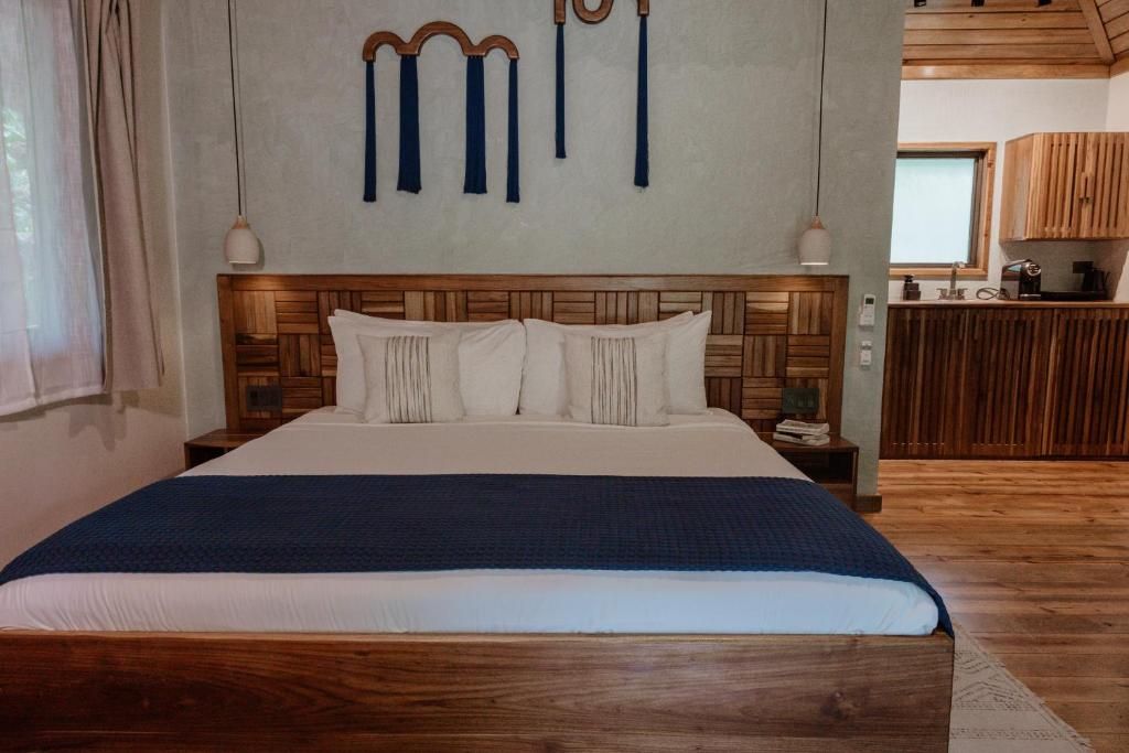 Cama king con cabecera de madera, almohadas blancas, camino azul marino y mesas de noche integradas en habitación luminosa con detalles de madera