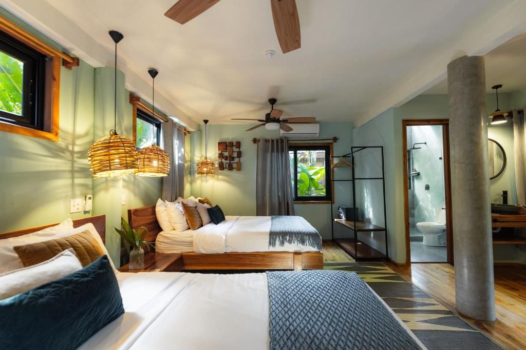Habitación con dos camas queen, lámparas de tejido, paredes verde salvia, muebles de madera, ventiladores de techo y vistas al jardín