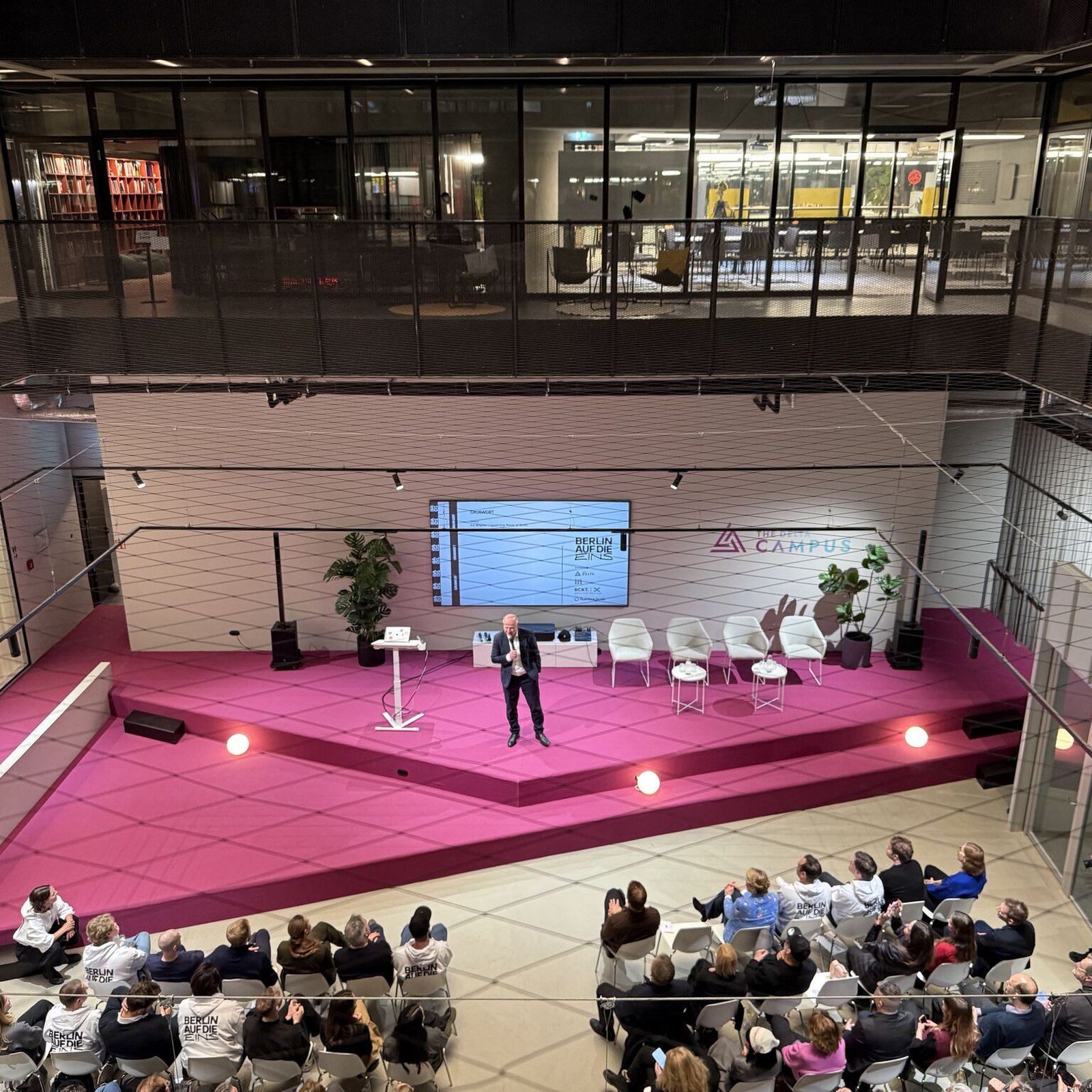 Speaker on the pink main stage of The Delta Campus in Berlin, seen from above, with a Berlin auf die Eins audience