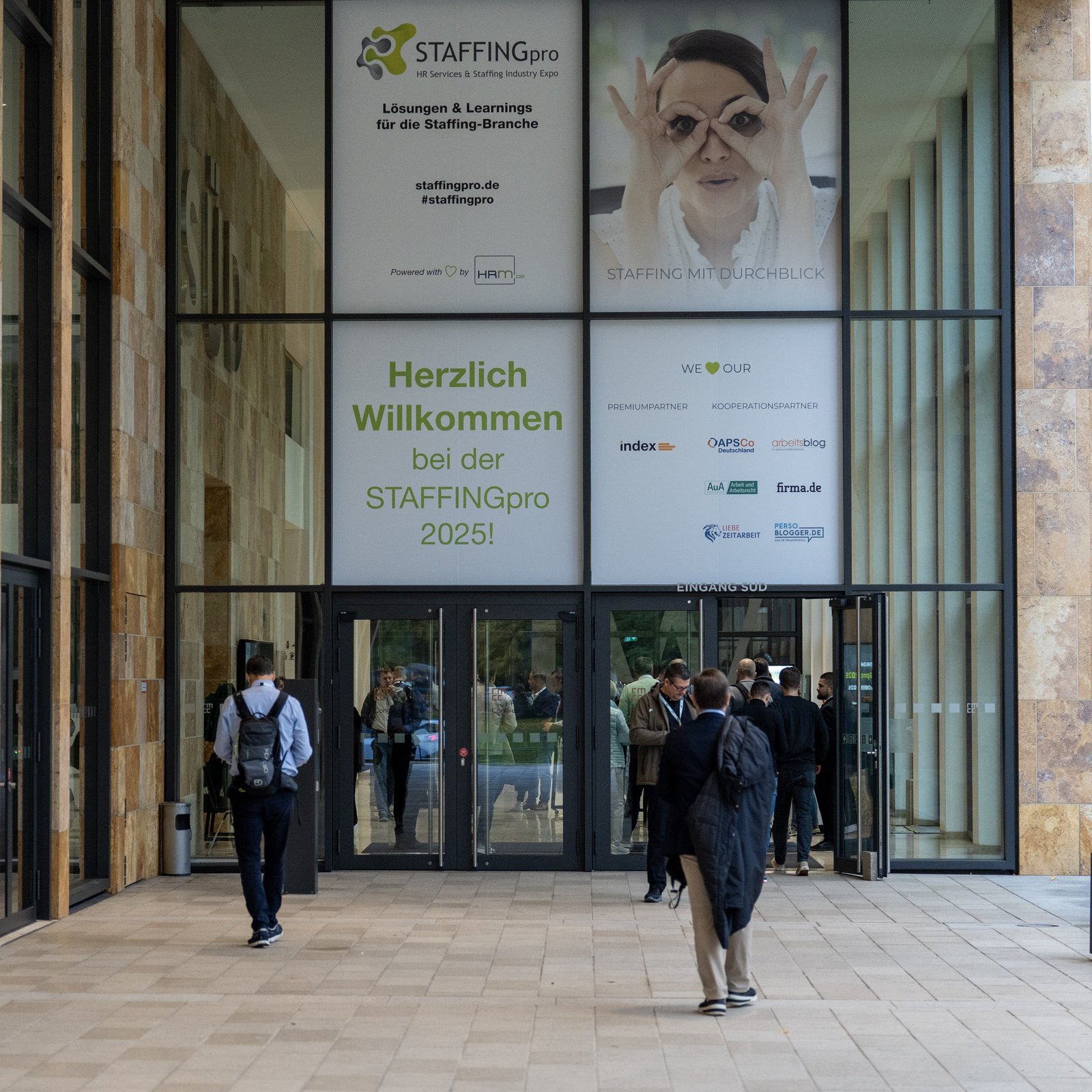 Visitors entering the RheinMain CongressCenter Wiesbaden under a STAFFINGpro 2025 welcome banner
