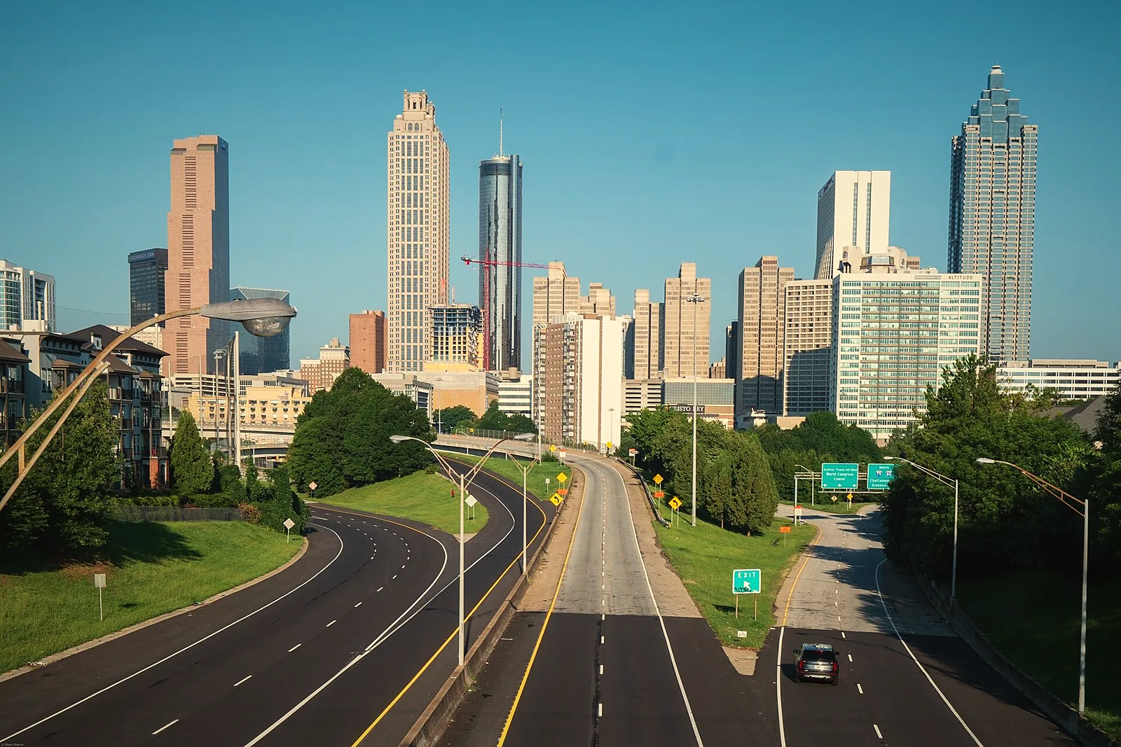 The downtown Atlanta skyline rising above a tree-lined freeway, seen from the Jackson Street Bridge