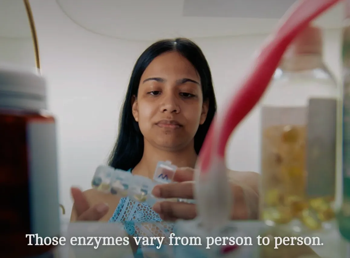 A woman with long black hair looks at a weekly pill organizer she is holding, surrounded by various bottles and containers, with the text caption 'Those enzymes vary from person to person.'