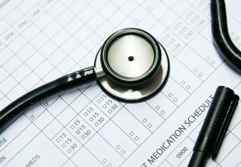 A stethoscope and a pen placed on a printed medication schedule form with checkboxes and time slots.