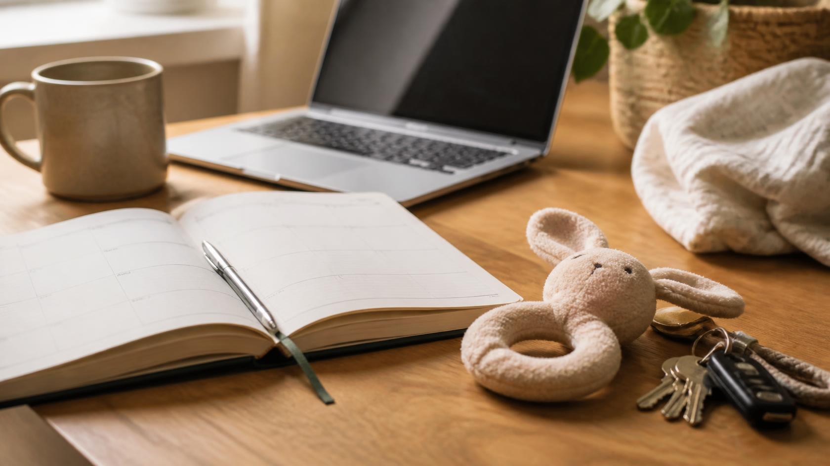 Bureau met een laptop, een open agenda en een babyknuffel naast een sleutelbos.