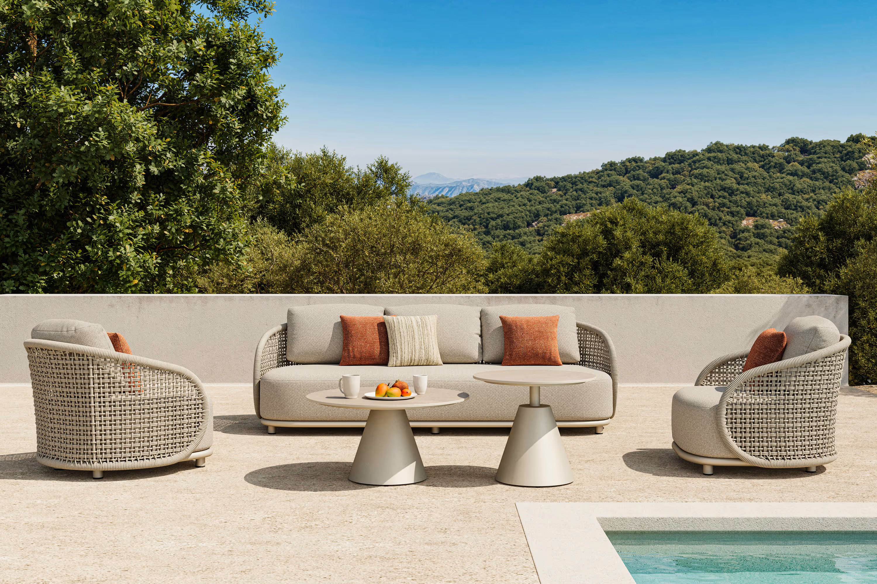 Set da salotto da esterno con divano e due poltrone in tessuto beige con cuscini arancioni, due tavolini tondi davanti e vista di alberi verdi e cielo azzurro.
