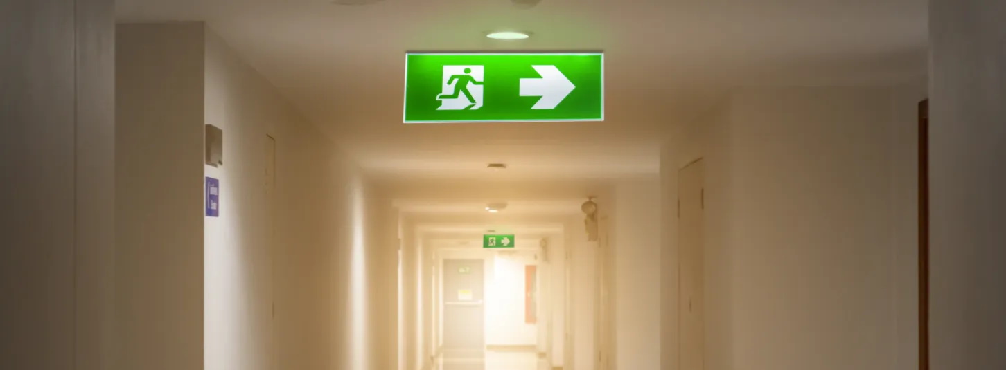 Illuminated green emergency exit sign along a building corridor