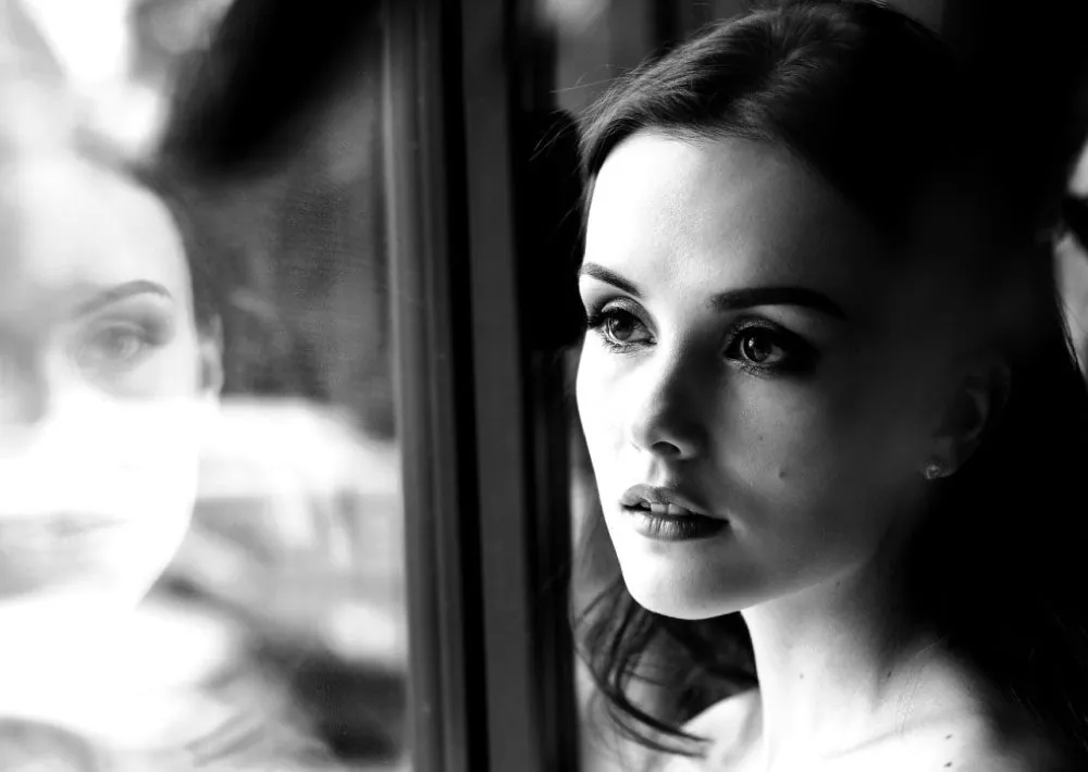 Black and white portrait of a woman looking out of a window