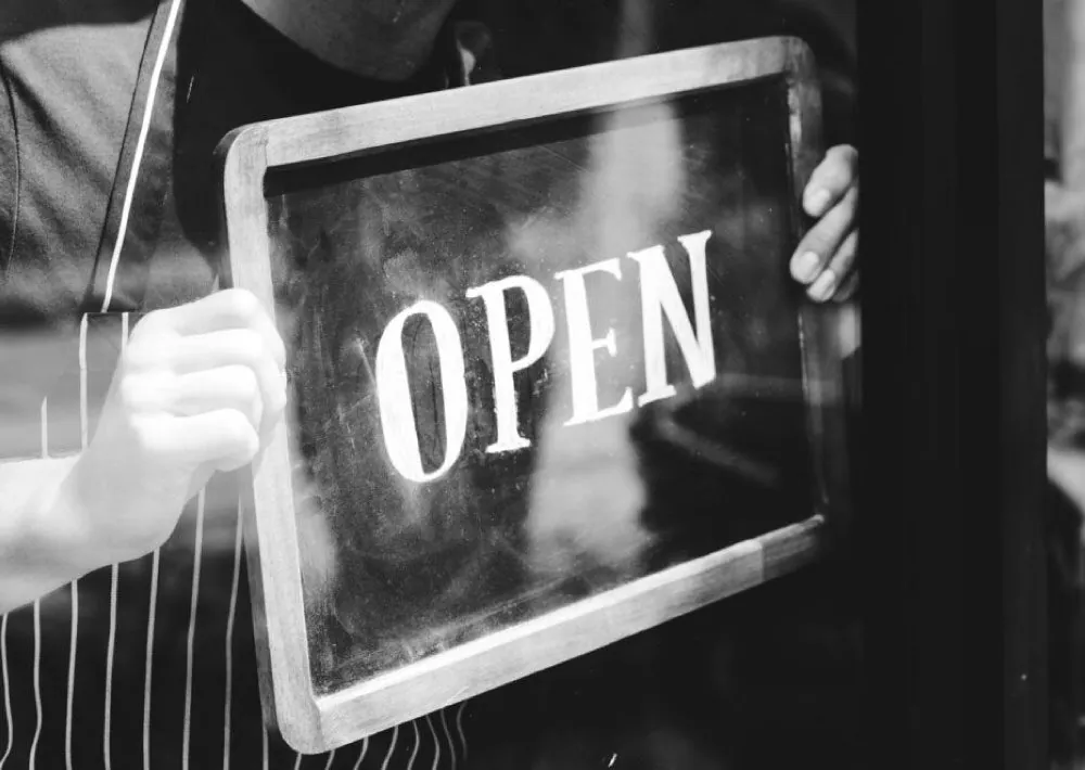 Black and white photo of a hand holding an Open sign in a shop window