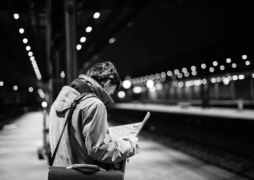 Black and white photo of a commuter reading a newspaper on a train platform