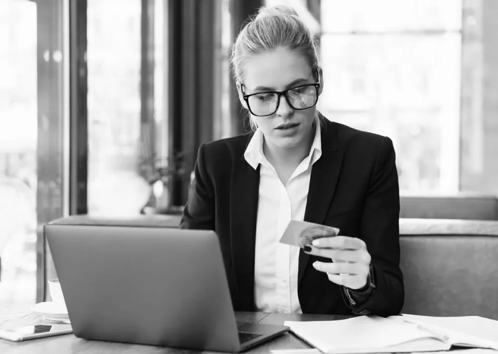 Black and white photo of a woman at a laptop holding a bank card